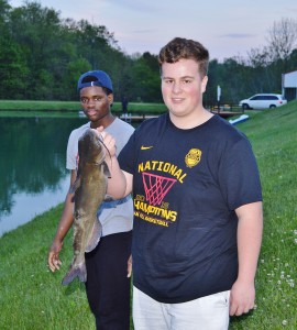 Two students lakeside, one holding a large fish