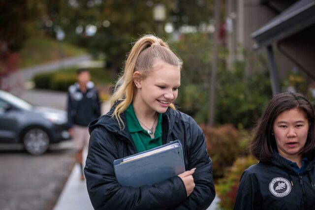 Female student in OHA uniform walking outside holding a book.