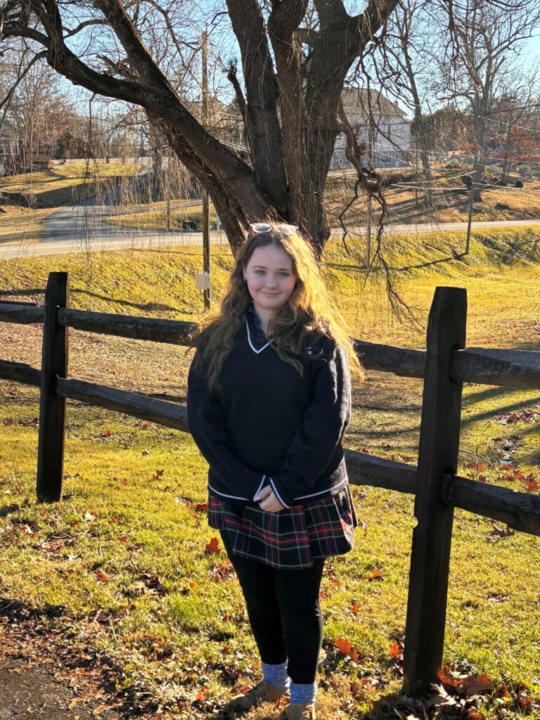 Senior Catie poses outsie near a wooden fence.